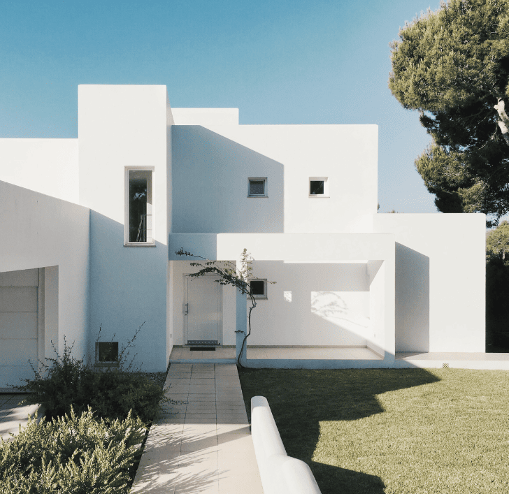 Fachada en blanco de una casa con formas cuadradas que evoca un estilo mediterráneo.