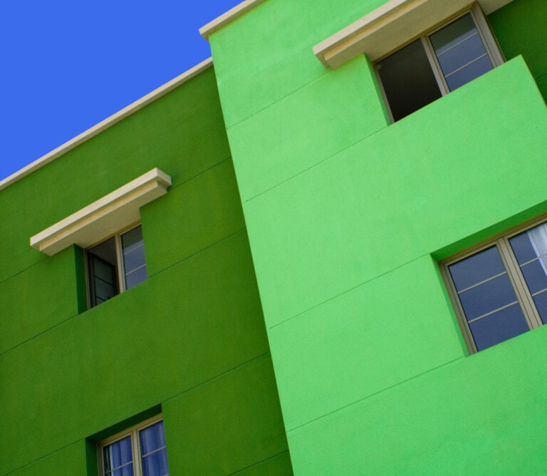 Fachada de un edificio en tonos verde oscuro y verde más claro que crea contraste y llama la atención. Vista aumentada de la fachada en dirección diagonal.