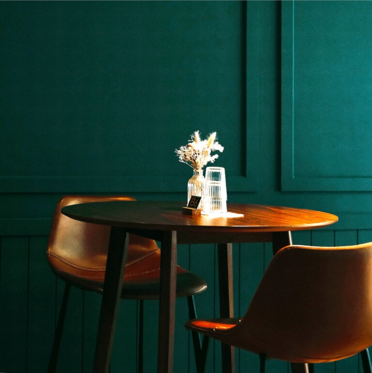 Interior de bar con una mesa y dos banquetas tapizadas en cuenta. Toda la pared pintada en color verde esmeralda oscuro